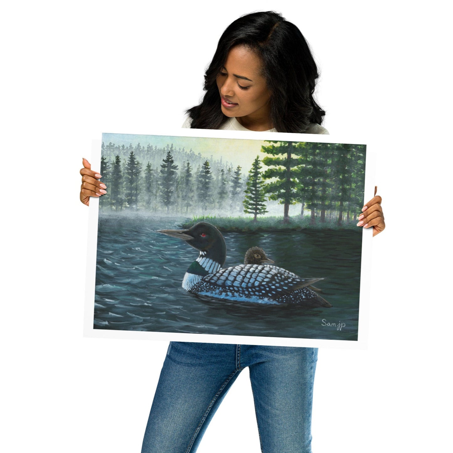 Woman holding a print of a loon and chick on a lake with trees in the background.